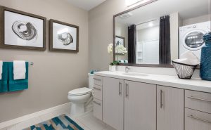 Image 28 - Apartments in Oakland, CA, for Rent - Baxter on Broadway - Bathroom with Large Vanity Mirrors, Tile Flooring, Washer and Dryer, and White Cabinets.